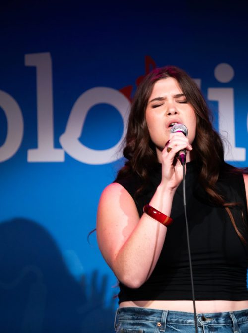 Woman-Singing-On-Stage-with-Her-Eyes-Closed-and-Hand-Raised-scaled